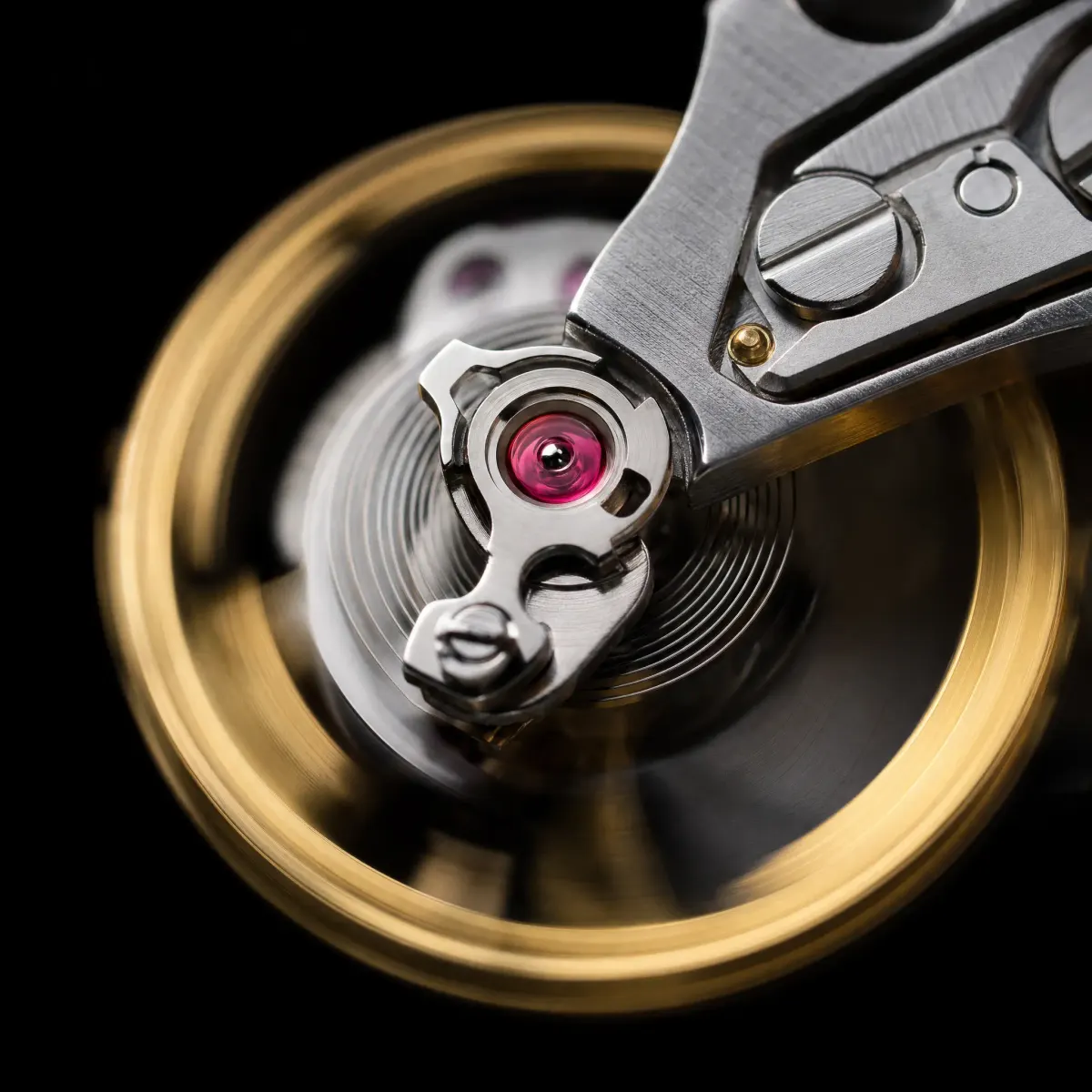 Watch balance wheel and hairspring in motion blur, its single jewel bearing glowing ruby red.