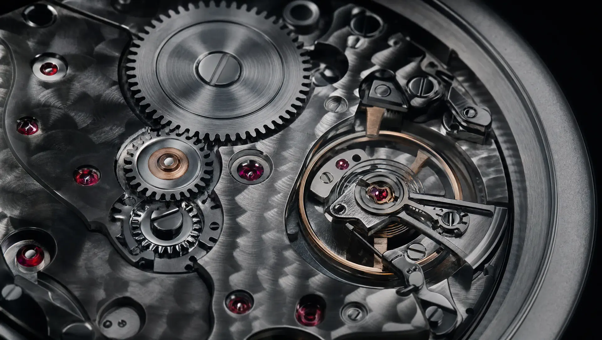 Extreme macro of a mechanical watch movement: meshing steel gears, engraved bridges and ruby jewel bearings.